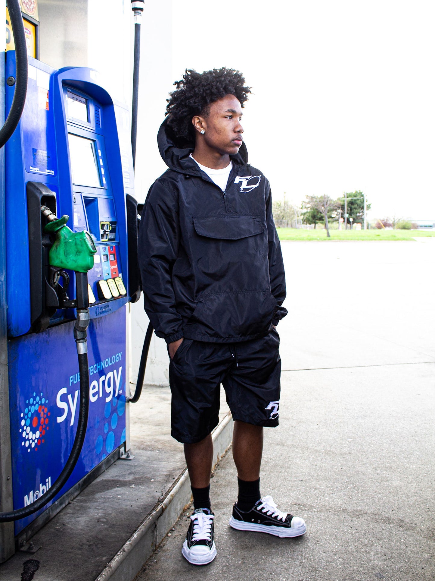 Person in a black raincoat standing next to a gas pump at a gas station.